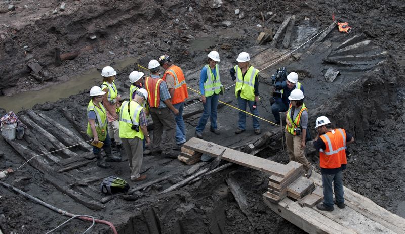 Workers and members of the media inspect the hull of a late 18th or early 19th century ship found at the World Trade Center site